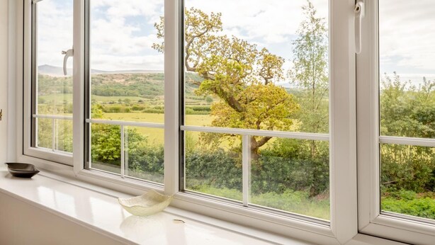 A room with a large window overlooking a green landscape with trees and hills.