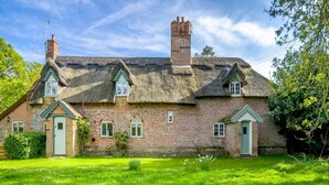 A traditional brick house with a thatched roof, multiple chimneys, and a well-maintained garden. - 2 Bed in Hanworth (oc-h32041) (Hanworth)