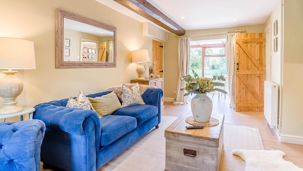 A living room with a blue sofa, a wooden coffee table, and a large mirror on the wall. - 2 Bed in Hanworth (oc-h32041) (Hanworth)