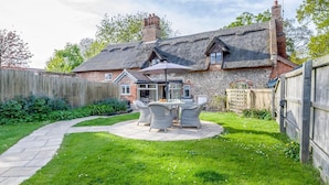 A house with a thatched roof, a patio with outdoor furniture, and a wooden fence. - 2 Bed in Hanworth (oc-h32041) (Hanworth)