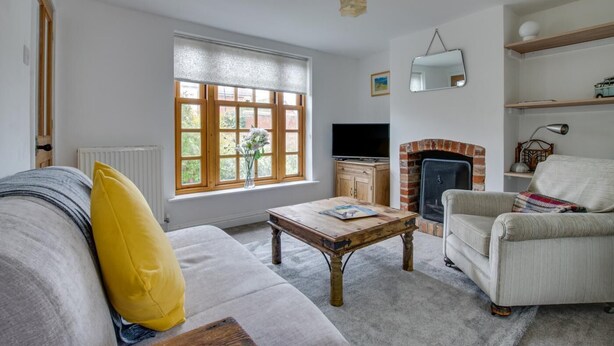 A living room with a sofa, armchair, coffee table, fireplace, television, and a window with a view of greenery. - 2 Bed in Aldeburgh (oc-3al) (Aldeburgh)