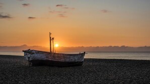 A boat on a pebbled beach with the sun setting in the background. - 2 Bed in Aldeburgh (oc-3al) (Aldeburgh)