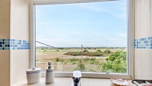 Een badkamer met uitzicht op een landelijk landschap door het raam, een wastafel, een zeepdispenser en een handdoekhouder.