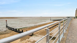 Een kustpad met een metalen hekwerk, een zandstrand en een verre horizon over de zee.