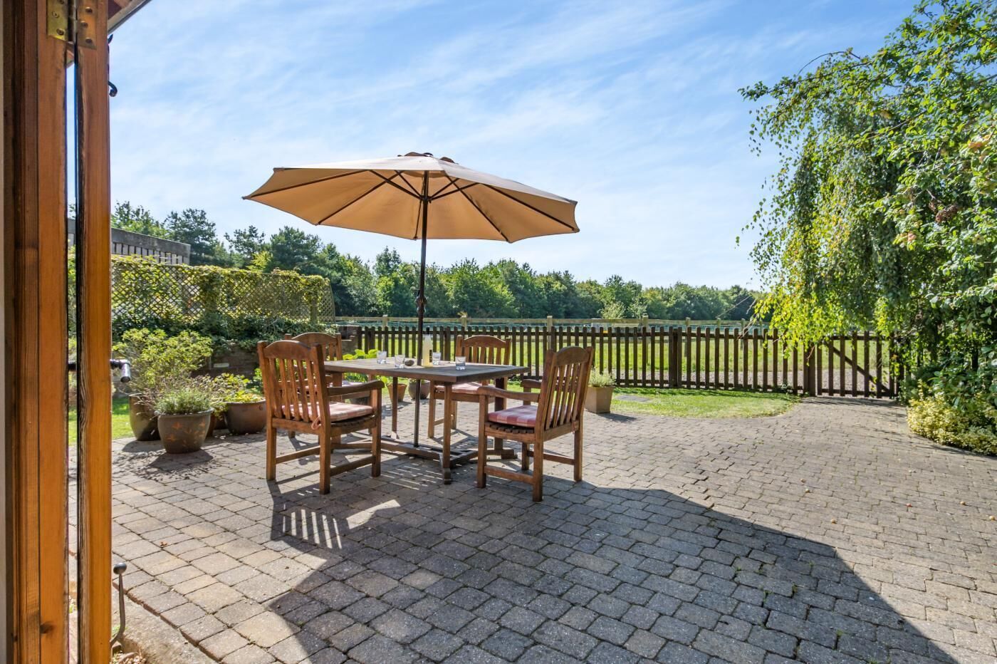 Une terrasse extérieure avec une table et des chaises, un grand parasol et une vue sur un jardin et une clôture.
