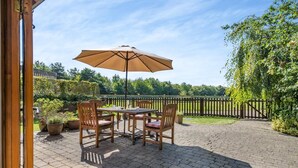 Eine Terrasse im Freien mit Tisch und Stühlen, einem großen Sonnenschirm und Blick auf Garten und Zaun.