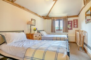 Une chambre avec deux lits, une commode en bois, une lampe et une fenêtre avec des rideaux.