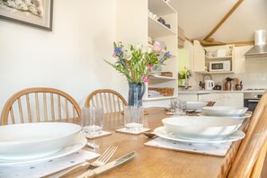 Une table à manger dressée avec des assiettes, des verres et des couverts, un vase rempli de fleurs, et une cuisine en arrière-plan.