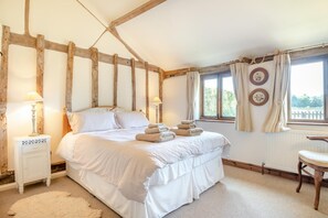 Een slaapkamer met een bed, twee nachtkastjes, een stoel, een raam met gordijnen en uitzicht op groen.