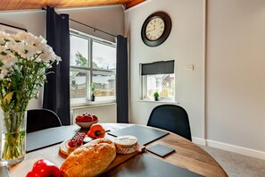 Un coin repas avec une table en bois, un panier de pommes, une miche de pain et une horloge au mur.