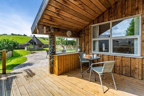 Une cabane en bois dotée d’une terrasse, d’un coin repas avec des chaises et une table, et offrant une vue sur un paysage verdoyant.