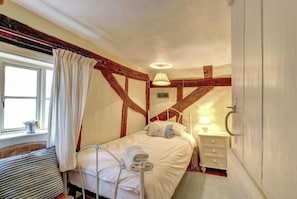 A bedroom with a bed, bedside table, lamp, and a window with curtains.