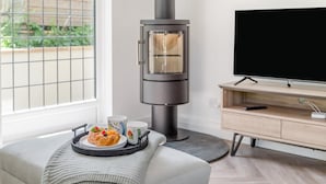 Ein modernes Wohnzimmer mit eingebautem Holzofen, einem Flachbildfernseher und einer Essecke mit einer Auswahl an Gebäck.