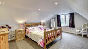 Ein Schlafzimmer mit einem hölzernen Bett, Nachttischen, einem Spiegel, einem Stuhl und einem Fenster mit Vorhängen.