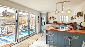A modern kitchen with a large island, sliding glass doors to a patio, and a view of a swimming pool. - 1 Bed in Beadnell (oc-s32097) (Beadnell)