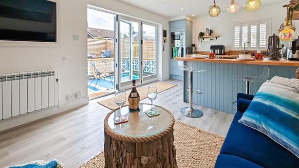 A modern kitchen with a bar area, a dining area with a round wooden table, and a cozy seating area with a blue sofa. - 1 Bed in Beadnell (oc-s32097) (Beadnell)
