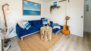 A living room with a blue sofa, a wooden coffee table, a guitar, and a painting of the ocean. - 1 Bed in Beadnell (oc-s32097) (Beadnell)