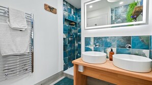 A modern bathroom with two white sinks, a wooden vanity, a towel rack with a white towel, and a mirror with a wooden frame. - 1 Bed in Beadnell (oc-s32097) (Beadnell)