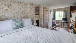 Ein Schlafzimmer mit Bett, Sessel, Schreibtisch, Spiegel und Kamin.
