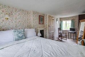 Ein Schlafzimmer mit Bett, Sessel, Schreibtisch, Spiegel und Kamin.