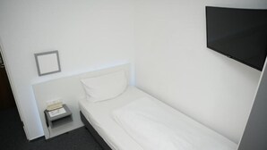 A small, single-bed room with a white bed, a small bedside table with a lamp, and a TV mounted on the wall. - Weber Residenz (Mannheim)