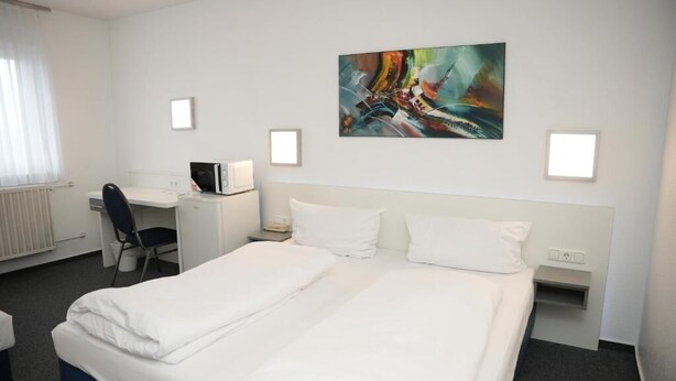 A hotel room with a double bed, a desk with a computer, a chair, and a painting on the wall. - Weber Residenz (Mannheim)