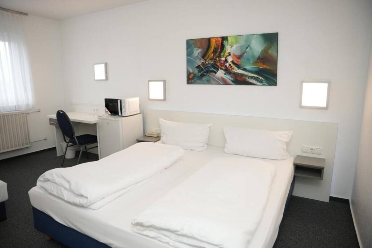 A hotel room with a double bed, a desk with a computer, a chair, and a painting on the wall.