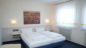 A hotel room with a bed, two bedside tables, a chair, a painting on the wall, and a window with curtains. - Weber Residenz (Mannheim)