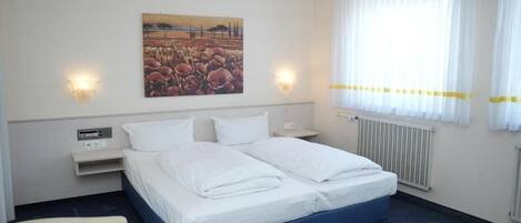 A hotel room with a bed, two bedside tables, a chair, a painting on the wall, and a window with curtains.