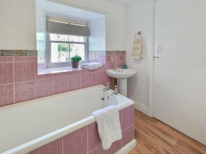 A bathroom with a bathtub, a sink, and a window with a view of greenery outside.