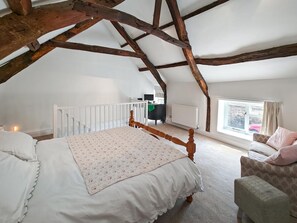 A bedroom with a wooden ceiling, a bed with a floral bedspread, a chair, and a window with curtains.
