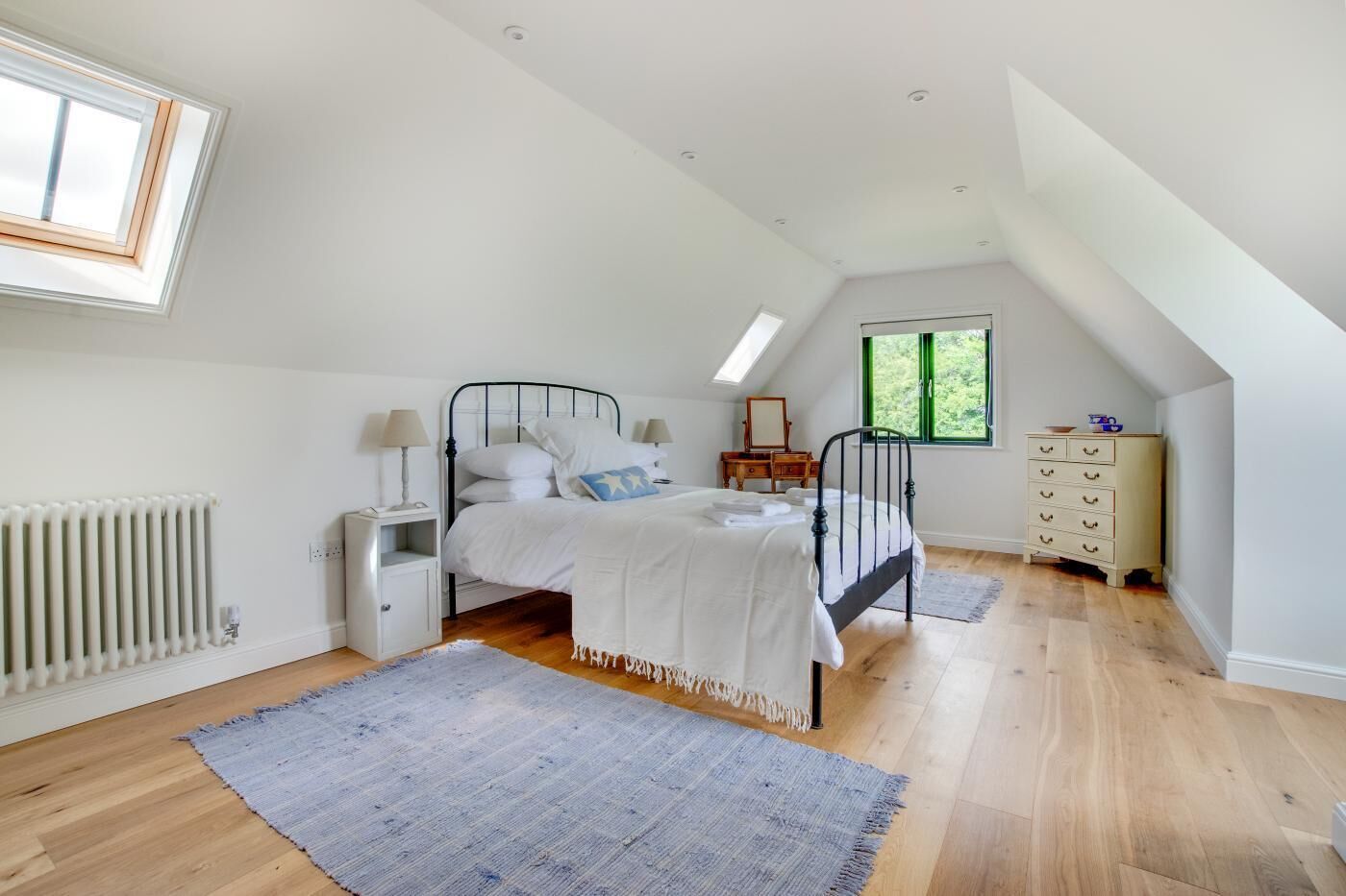 A bedroom with a bed, bedside tables, a dresser, a radiator, a window, and a skylight.