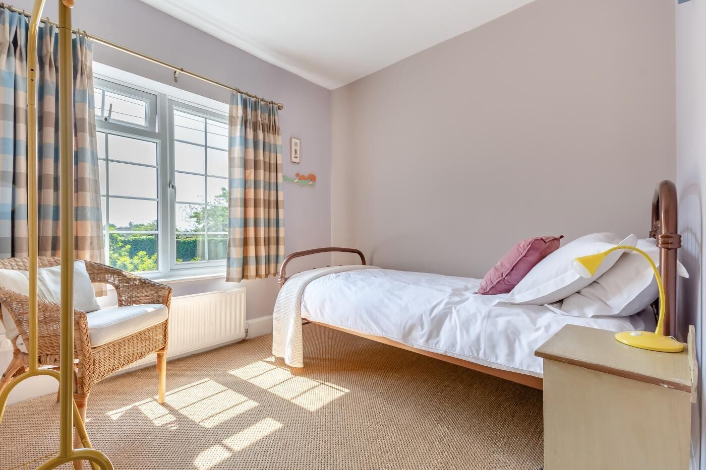 A bedroom with a bed, a wicker chair, a radiator, and a window with curtains.