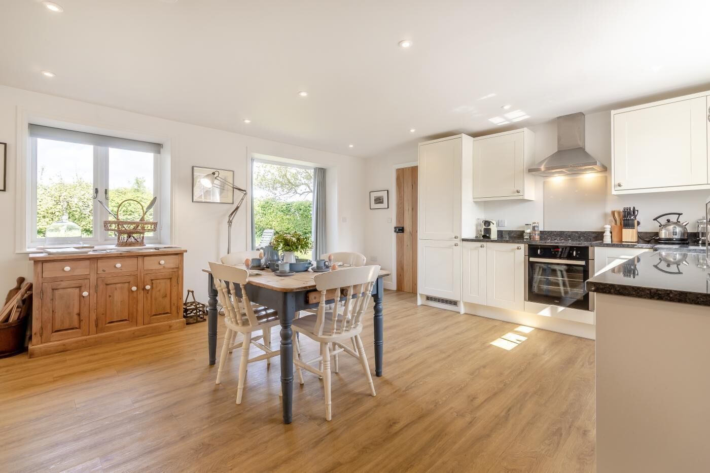 A modern kitchen with wooden cabinets, a dining area with chairs, and a large window providing natural light.
