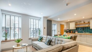 Un salon moderne avec un canapé gris, une petite table d’appoint et un coin repas agrémenté d’une nappe verte.