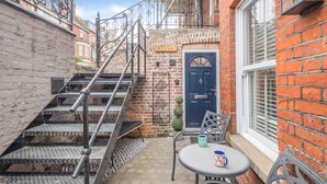 Une ruelle étroite avec un escalier en métal menant à une porte, une petite table avec une tasse et une chaise.