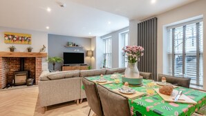 Un salon moderne avec une cheminée, un téléviseur et un coin repas où la table est mise pour le petit-déjeuner.