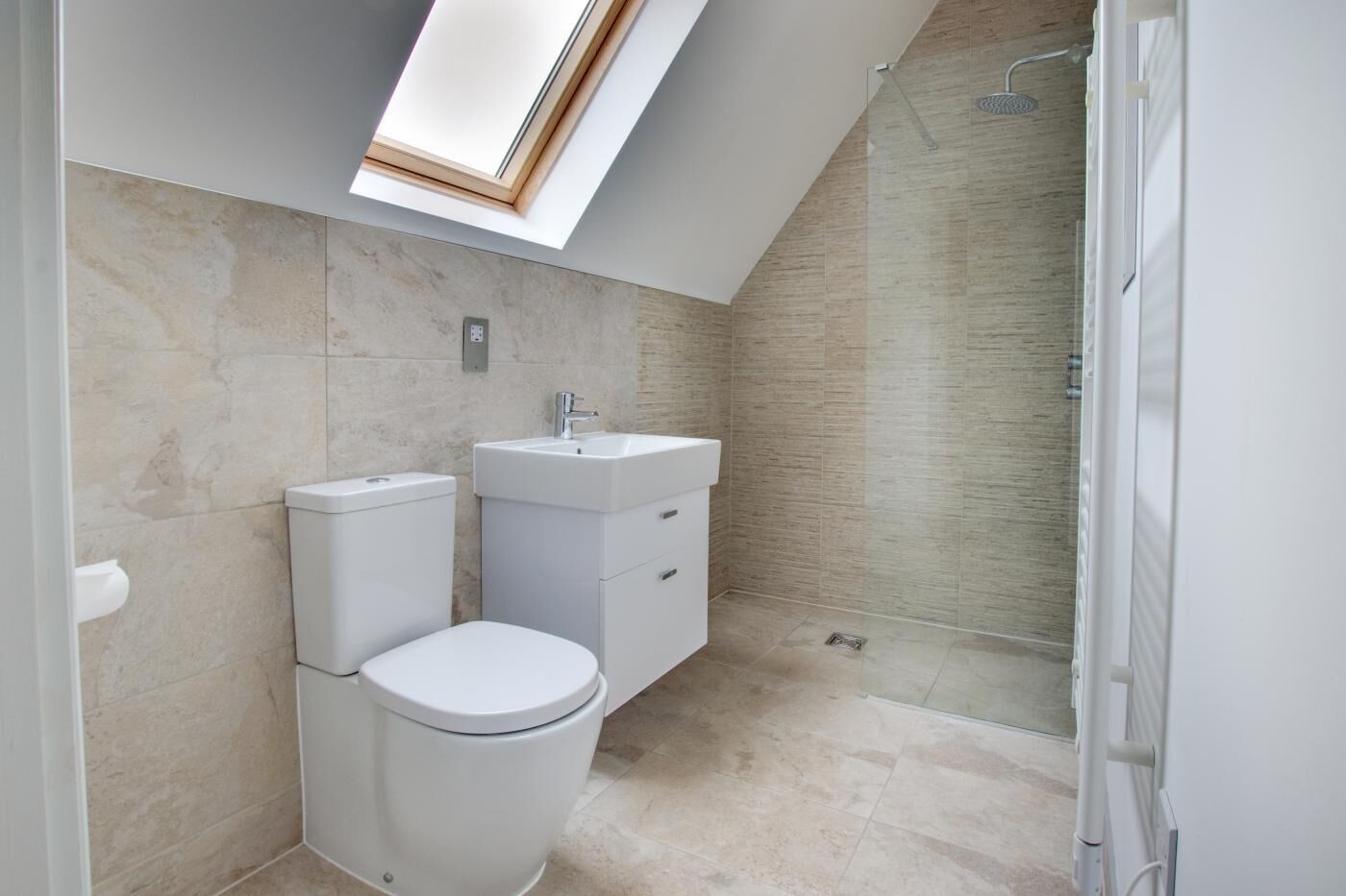 A modern bathroom with a skylight, a toilet, a sink, and a shower.