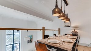 Zona pranzo con tavolo in legno apparecchiata per quattro persone, illuminazione a sospensione e una finestra vista esterna.