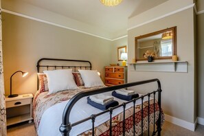 A bedroom with a bed, bedside table, lamp, dresser, mirror, and a shelf with decorative items. - 2 Bed in Dymchurch (oc-s31998) (Dymchurch)
