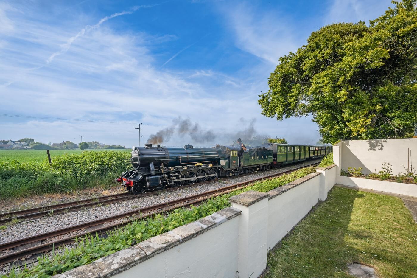 Eine Dampflokomotive auf Gleisen mit einer weißen Mauer und Grünpflanzen an einer Seite.