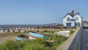 En byggnad vid kusten, döpt till ”Gamla Neptunus”, med fri utsikt över havet och vindkraftverk i bakgrunden.