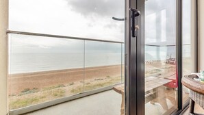 A balcony with a glass door, a view of the beach, and a wicker chair.