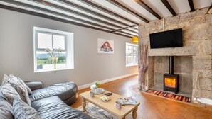 Ein Wohnzimmer mit Kamin aus Stein, einem Sofa, einem Couchtisch und einem an der Wand montierten Fernseher.
