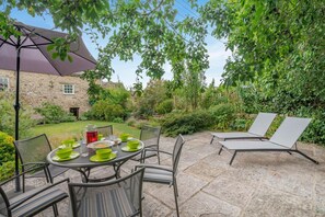 Eine Terrasse im Freien mit Esstisch und Stühlen, beschattet durch einen großen Sonnenschirm.