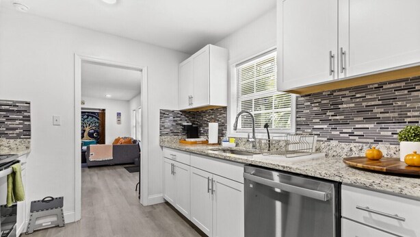 A modern kitchen with white cabinets, a granite countertop, and a backsplash with gray tiles. - The Gator Den: Perfect for Groups & Families! 3 BR/ 2 Bath (Gainesville)