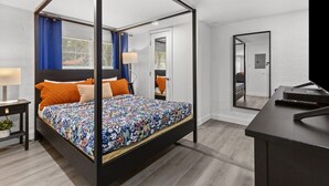 A four-poster bed with a floral bedspread, a bedside table with a lamp, and a large mirror on the wall. - The Gator Den: Perfect for Groups & Families! 3 BR/ 2 Bath (Gainesville)