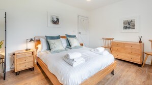 Ein ordentlich eingerichtetes Schlafzimmer mit Bett, Nachttischen, einer Kommode und Kunstwerken an den Wänden.