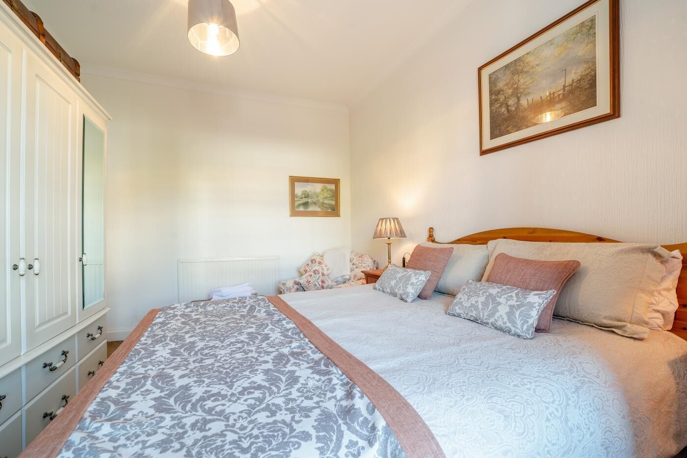 A bedroom with a large bed, a wardrobe, a nightstand, and a painting on the wall.