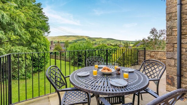 A round metal table with chairs on a balcony, overlooking a lush green landscape with hills. - 3 Bed in Hawes (oc-ds967) (Hawes)
